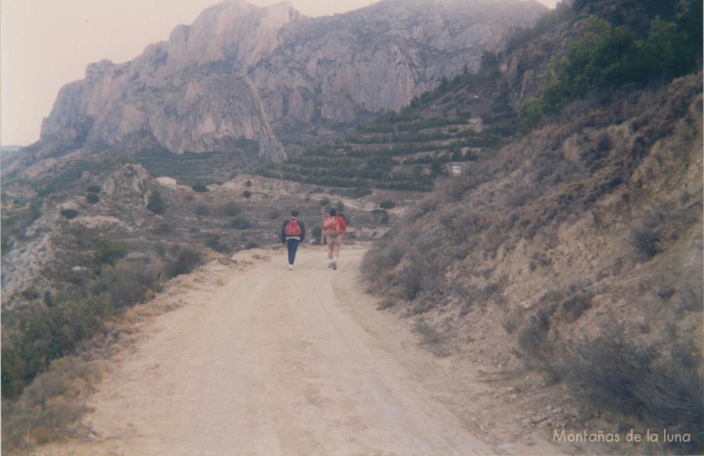 Camino del Racó de La Seva, delante las paredes de la Penya de l'Home a la izquierda, y junto al camino la Casa del Suizo o Casa Gorjas